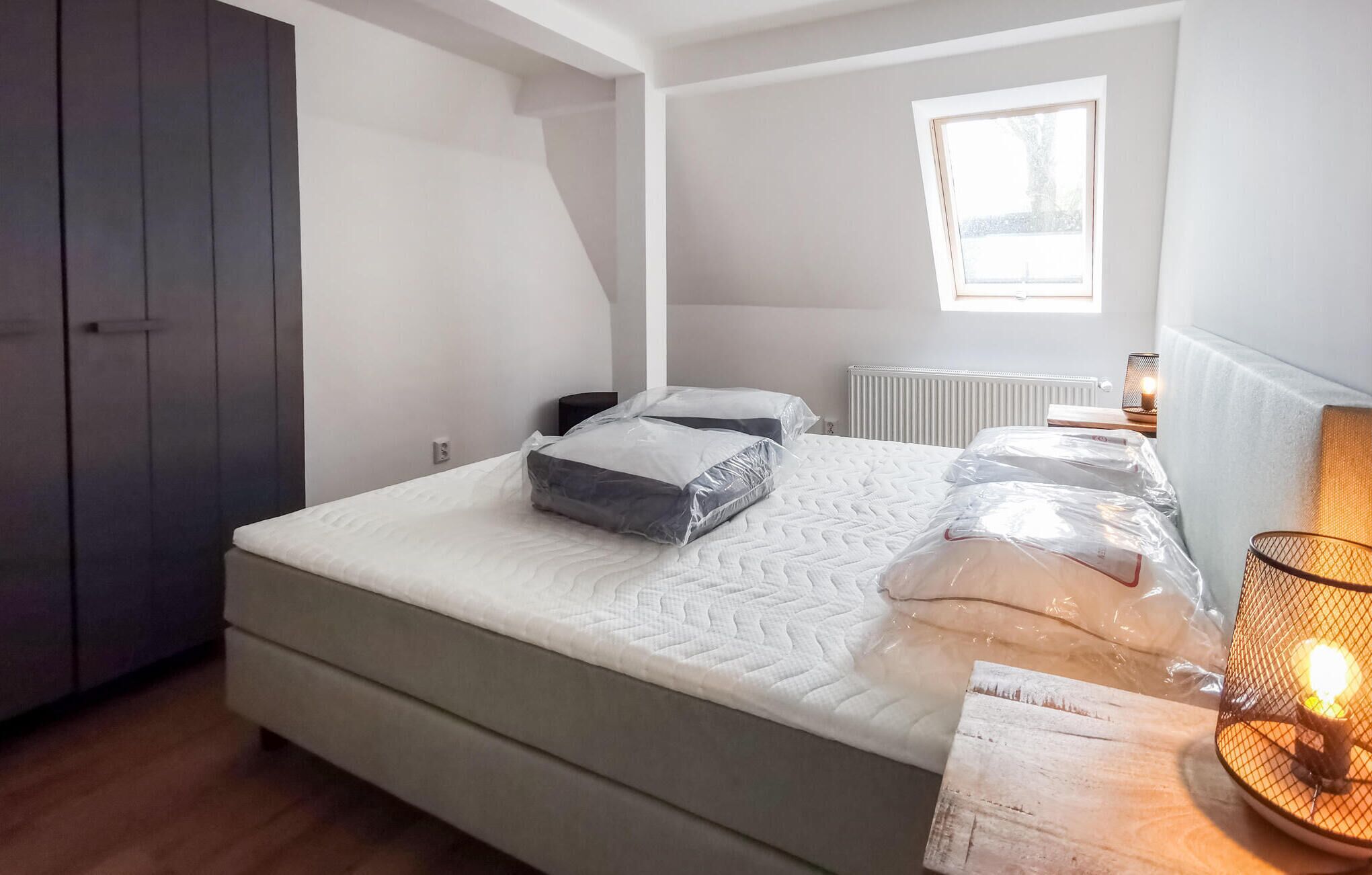 A bedroom with a bed, a window, a radiator, and a wardrobe.