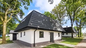 En moderne bygning med sort tag og hvide vægge, der har en lille indgang og en belagt indkørsel.