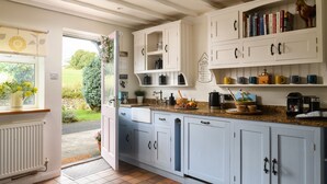 A kitchen with light blue cabinets, a countertop with various kitchen items, and a view of the garden through an open door. - Ty Bach - Beaumaris (Beaumaris)