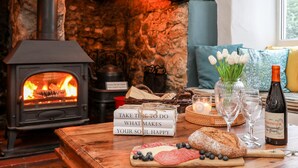 A cozy room with a stone fireplace, a wooden table with books, bread, and cheese, and a bottle of wine. - Ty Bach - Beaumaris (Beaumaris)