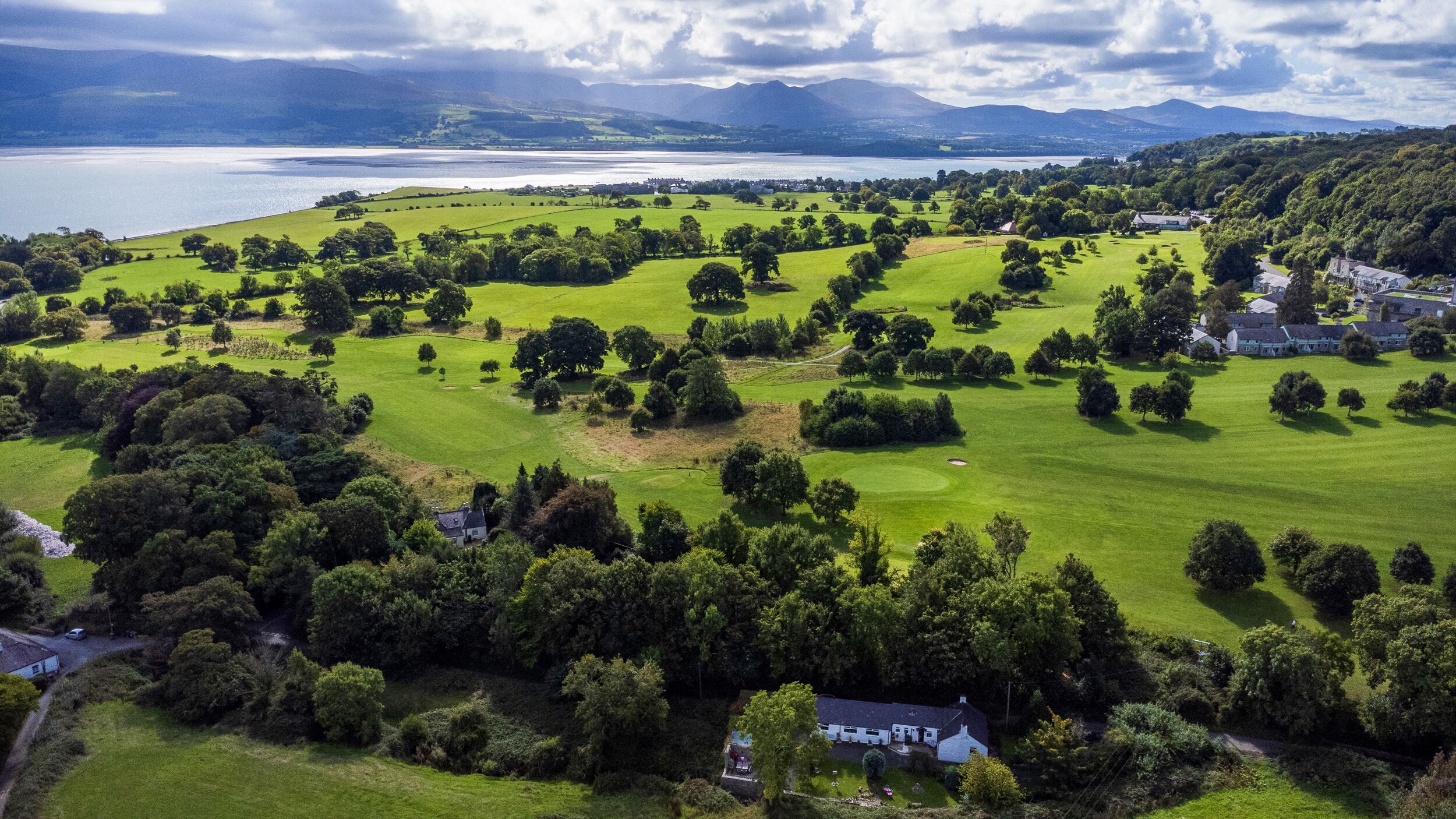 An aerial view of a golf course with a lake and mountains in the background.