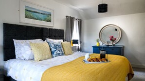 A neatly made bed with a yellow blanket, a bedside table with a coffee pot, and a framed picture on the wall. - Ty Bach - Beaumaris (Beaumaris)