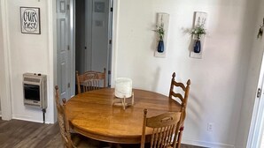 A dining area with a round wooden table, four wooden chairs, a white table lamp, and two wall-mounted planters with flowers. - Hummingbird Haven-3 Bed 2 Bath River House (Clifton)
