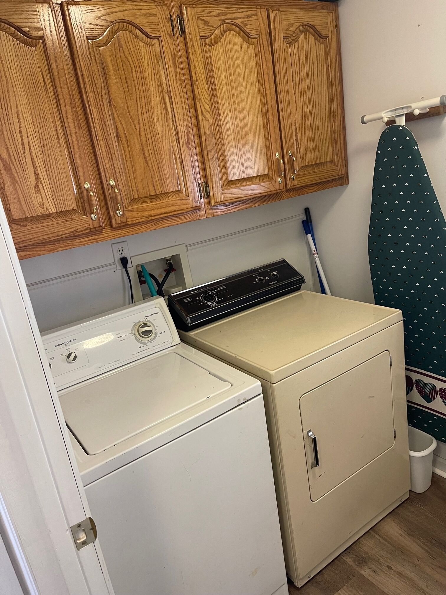 A laundry area with a washing machine, dryer, wooden cabinets, and an ironing board.