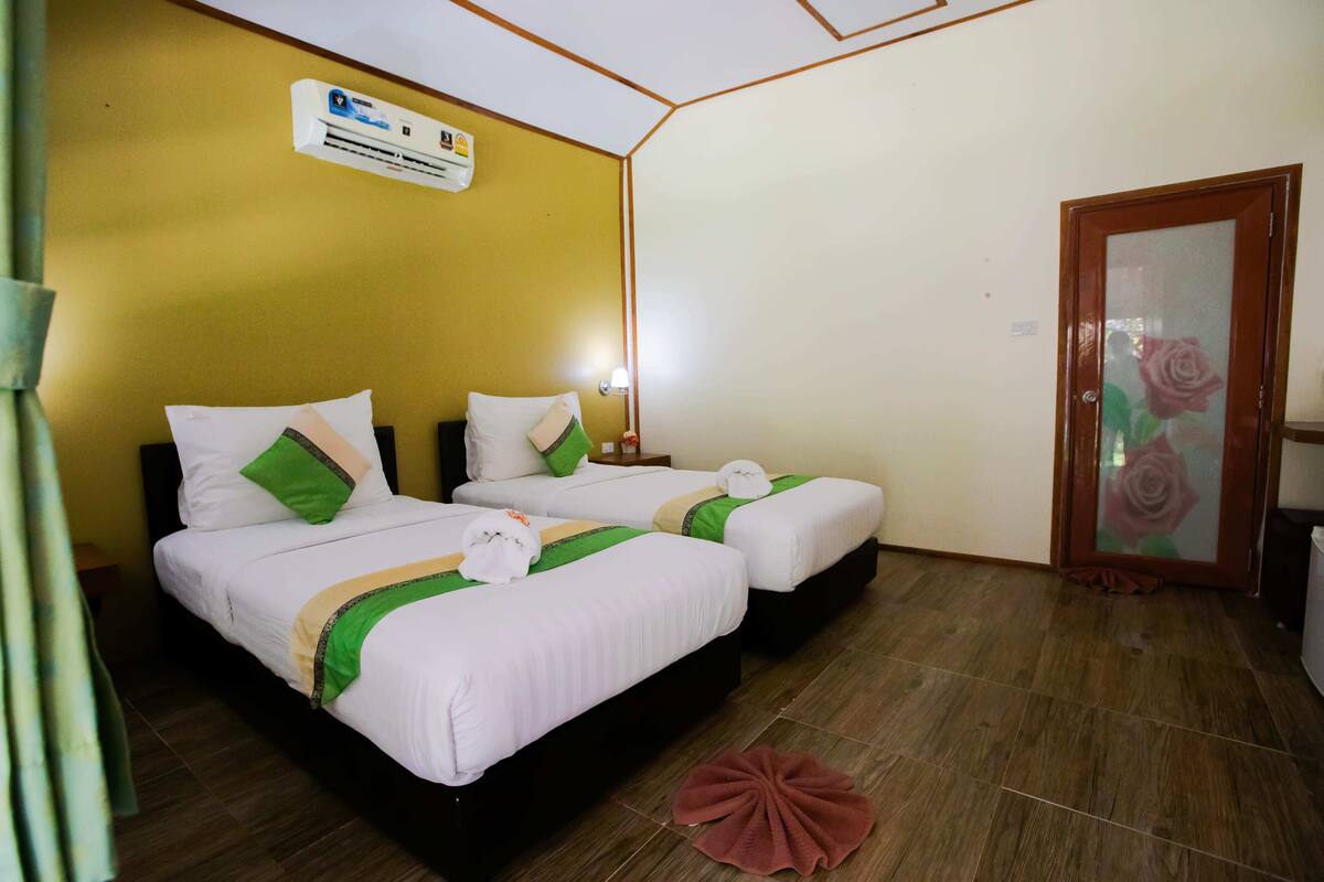 Habitación de hotel con dos camas, piso de madera, pared amarilla y una puerta con decoración de rosa.