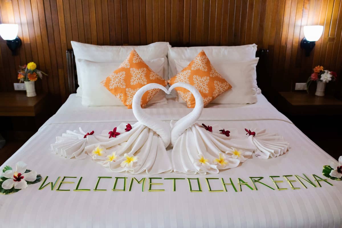Habitación de hotel con una cama decorada con un arreglo de toallas con forma de corazón y la inscripción 'WELCOME TO CHAREENA' en la colcha.