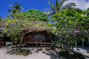 A wooden house with a tiled roof, surrounded by lush greenery and palm trees.