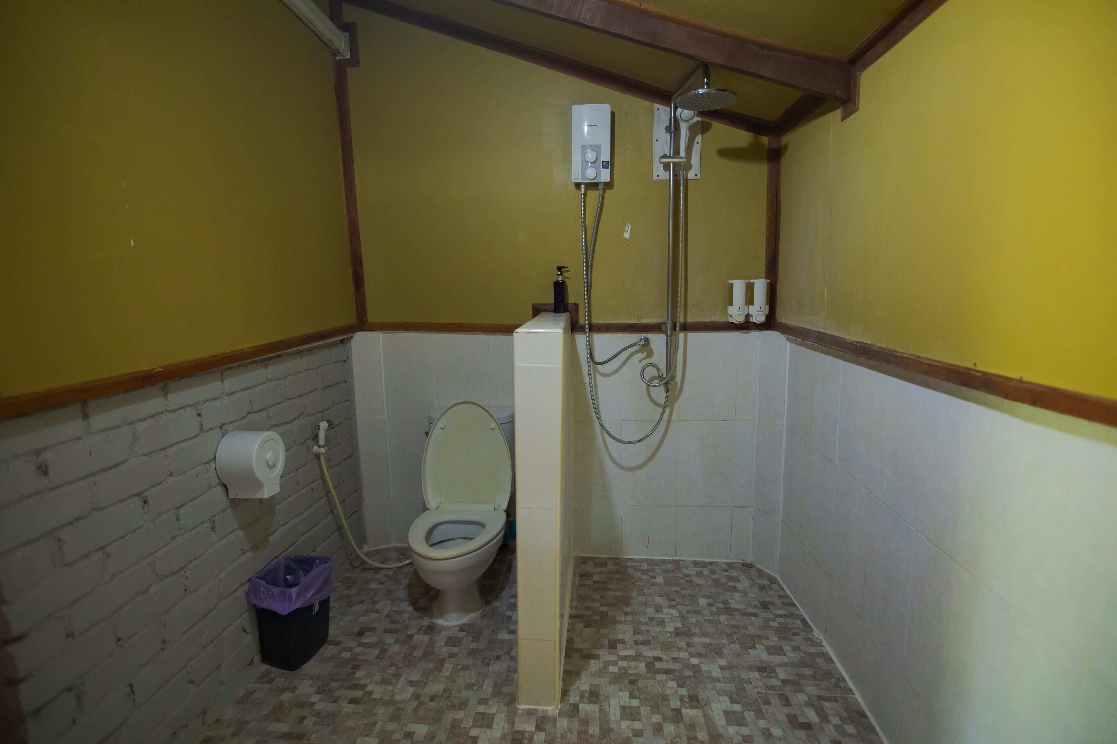 A small bathroom with a toilet, a shower, and a trash bin.