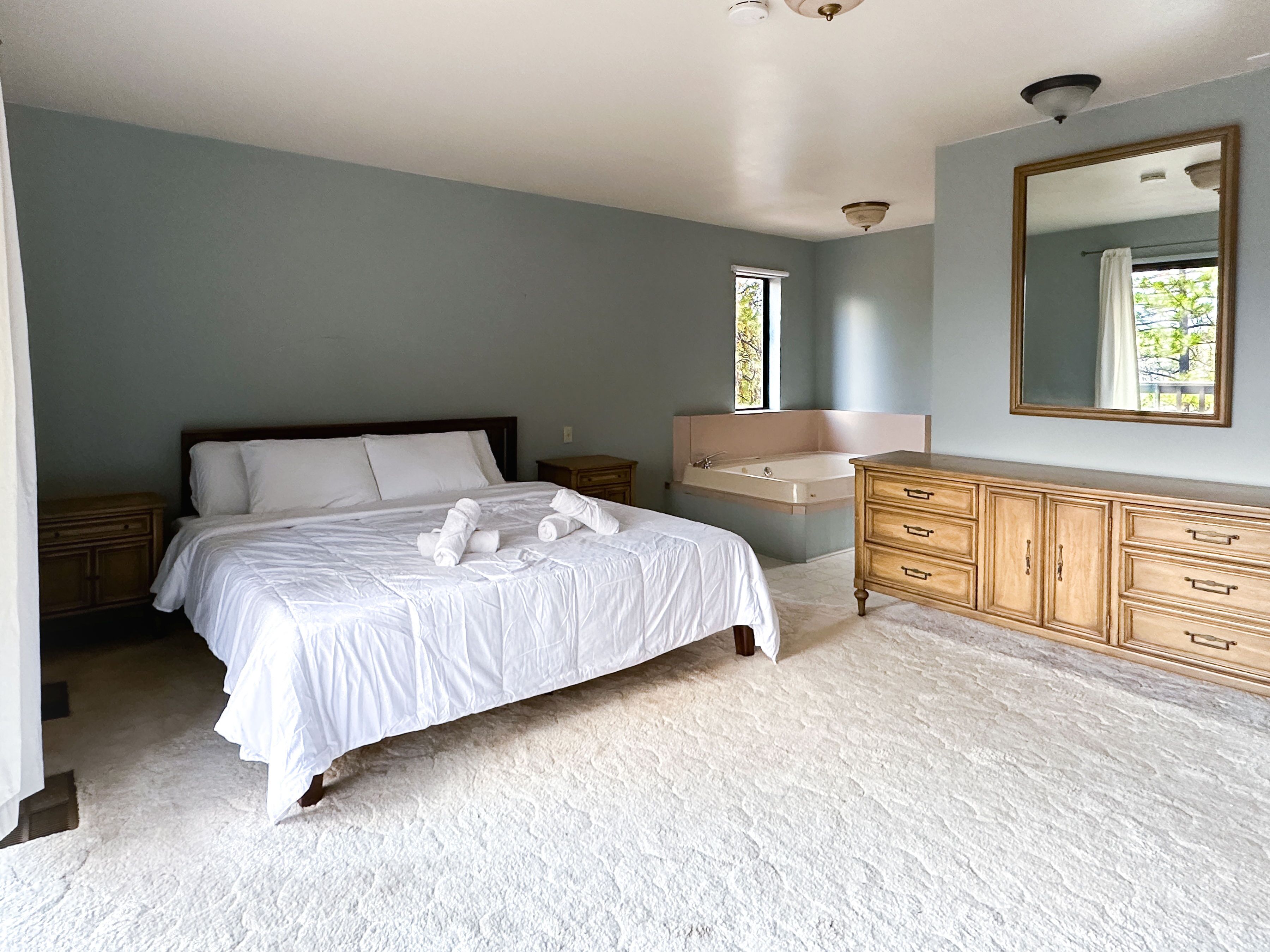 Une chambre à coucher avec un grand lit, une commode en bois, une coiffeuse avec un miroir et une fenêtre.