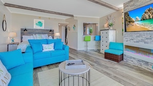 A modern living room with a blue sofa, a round coffee table, and a flat-screen TV mounted on a stone wall.