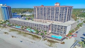 A large hotel with multiple floors, a swimming pool, and a parking area.