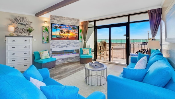 A modern living room with blue sofas, a fireplace, and a balcony with a view of the beach.