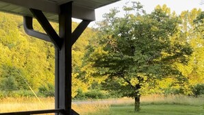 Une terrasse en bois avec une rambarde donnant sur un champ verdoyant et des arbres.