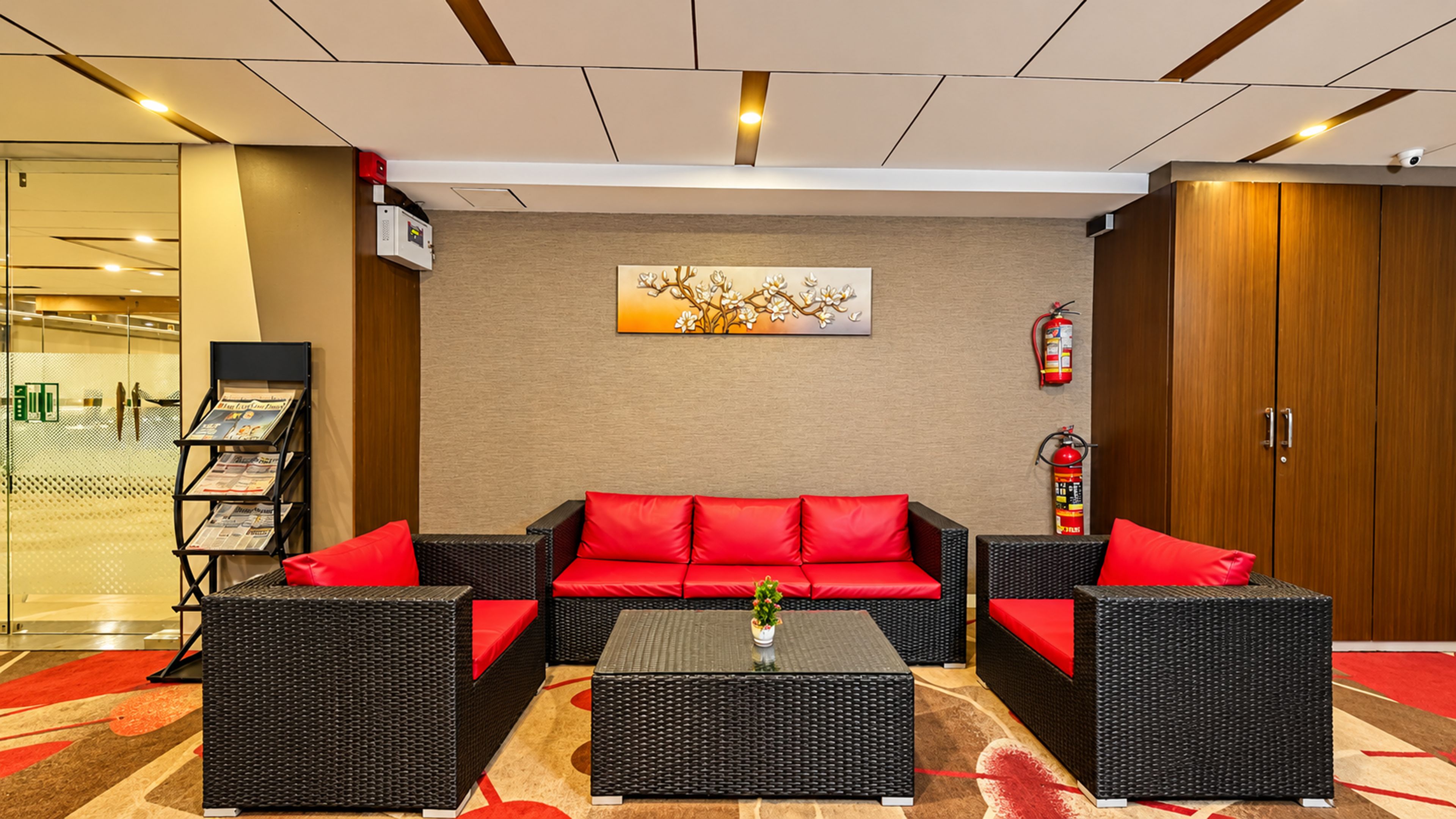 A lobby with a red sofa set, black wicker furniture, a fire extinguisher, and a wall-mounted fire alarm.
