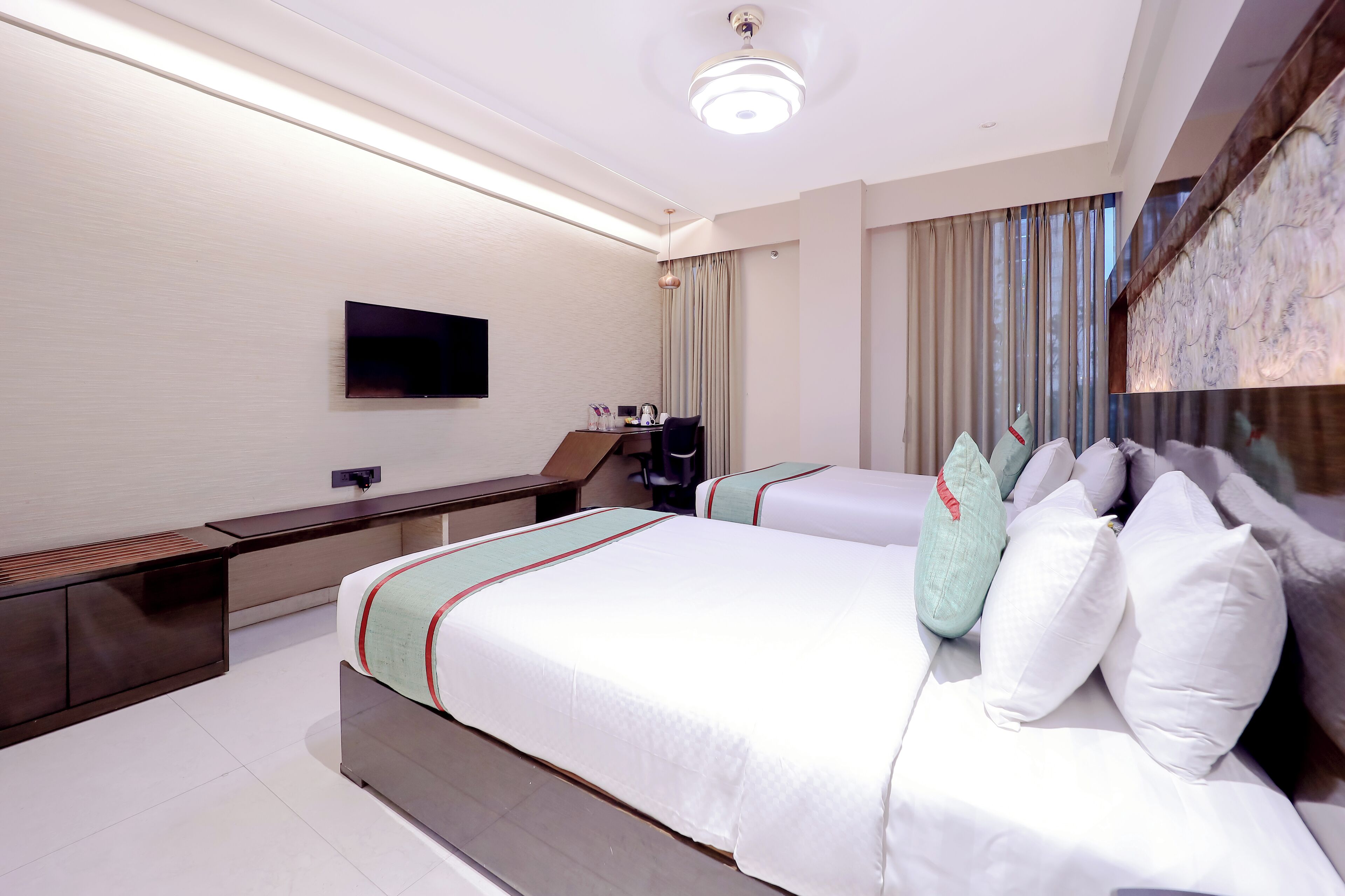 Een moderne hotelkamer met een groot bed, nachtkastjes, een flatscreen televisie en een groot raam met gordijnen.