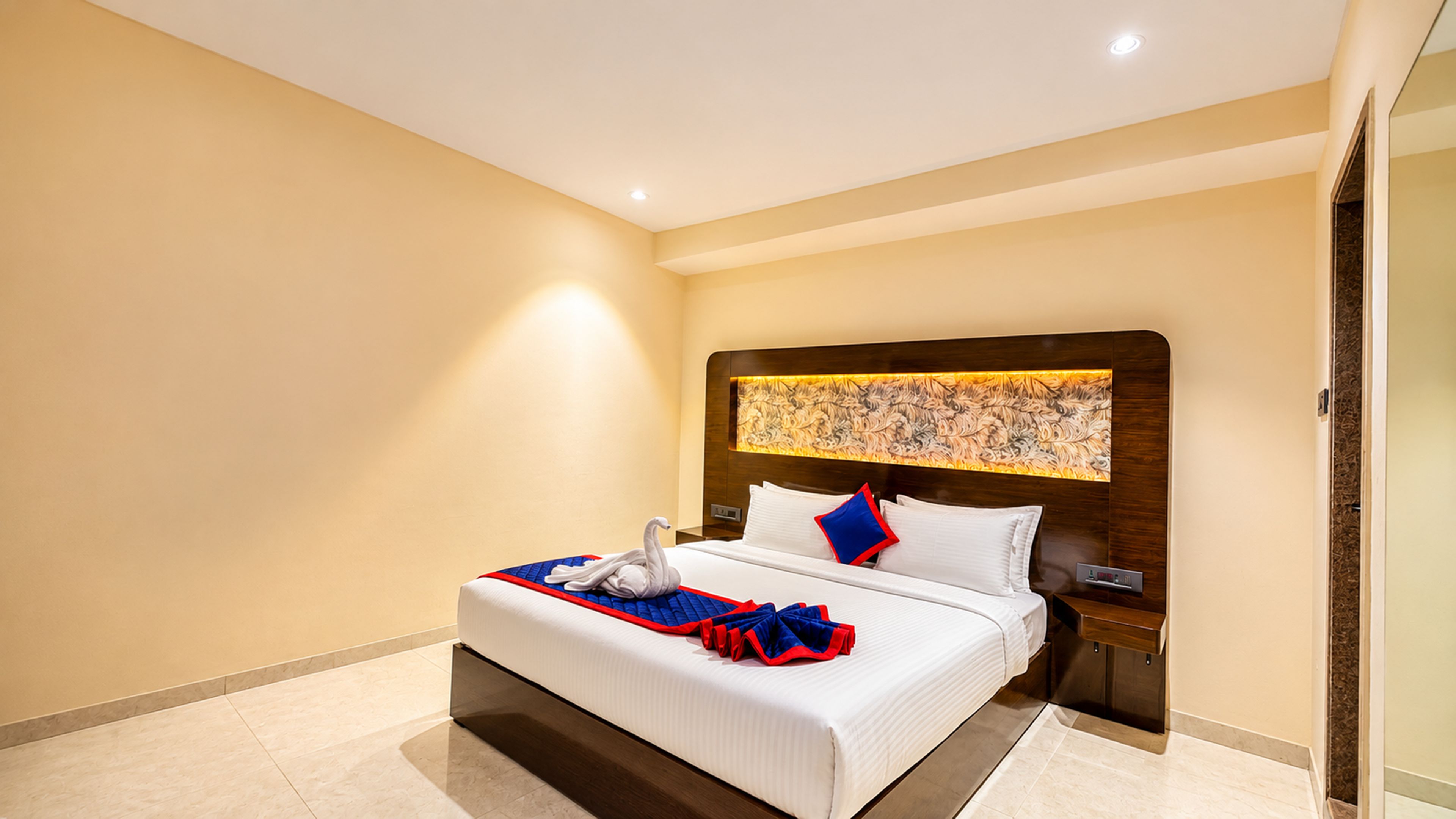 A hotel room with a large bed, a headboard with a decorative panel, a nightstand, and a wall-mounted artwork.