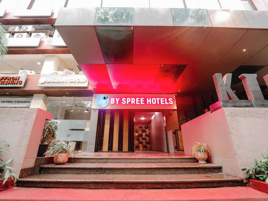 Entrada de un hotel con un letrero iluminado en rojo para By Spree Hotels, un letrero de Saffron Furnishing y una gran estructura en forma de 'K'.