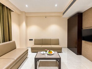 A modern living room with a sofa, a coffee table with fruit, and a flat-screen TV mounted on the wall. -  Zip By Spree Hotels Surat (Surat)