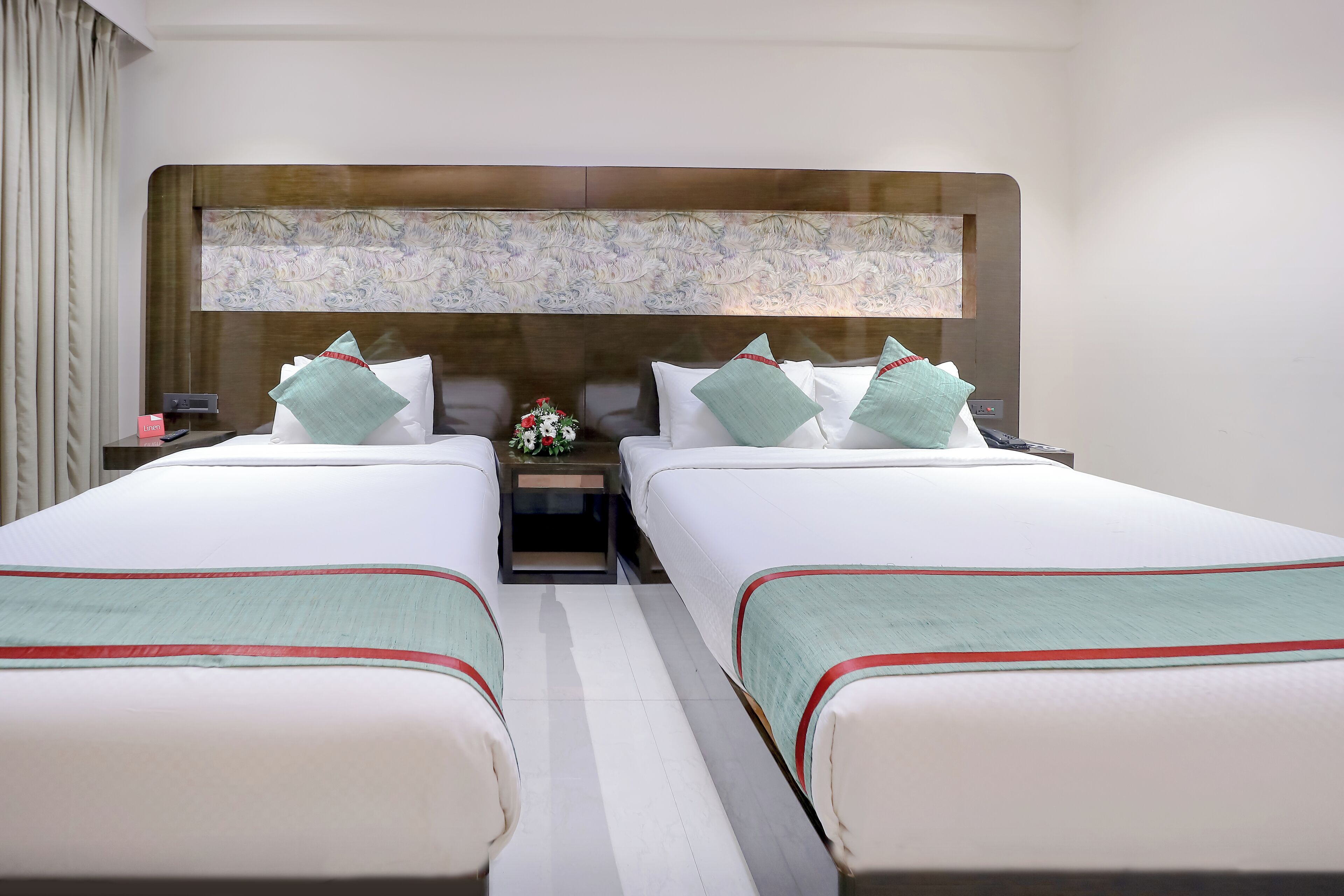 Una habitación de hotel con dos camas, una mesita de noche, una lámpara y un arreglo floral.