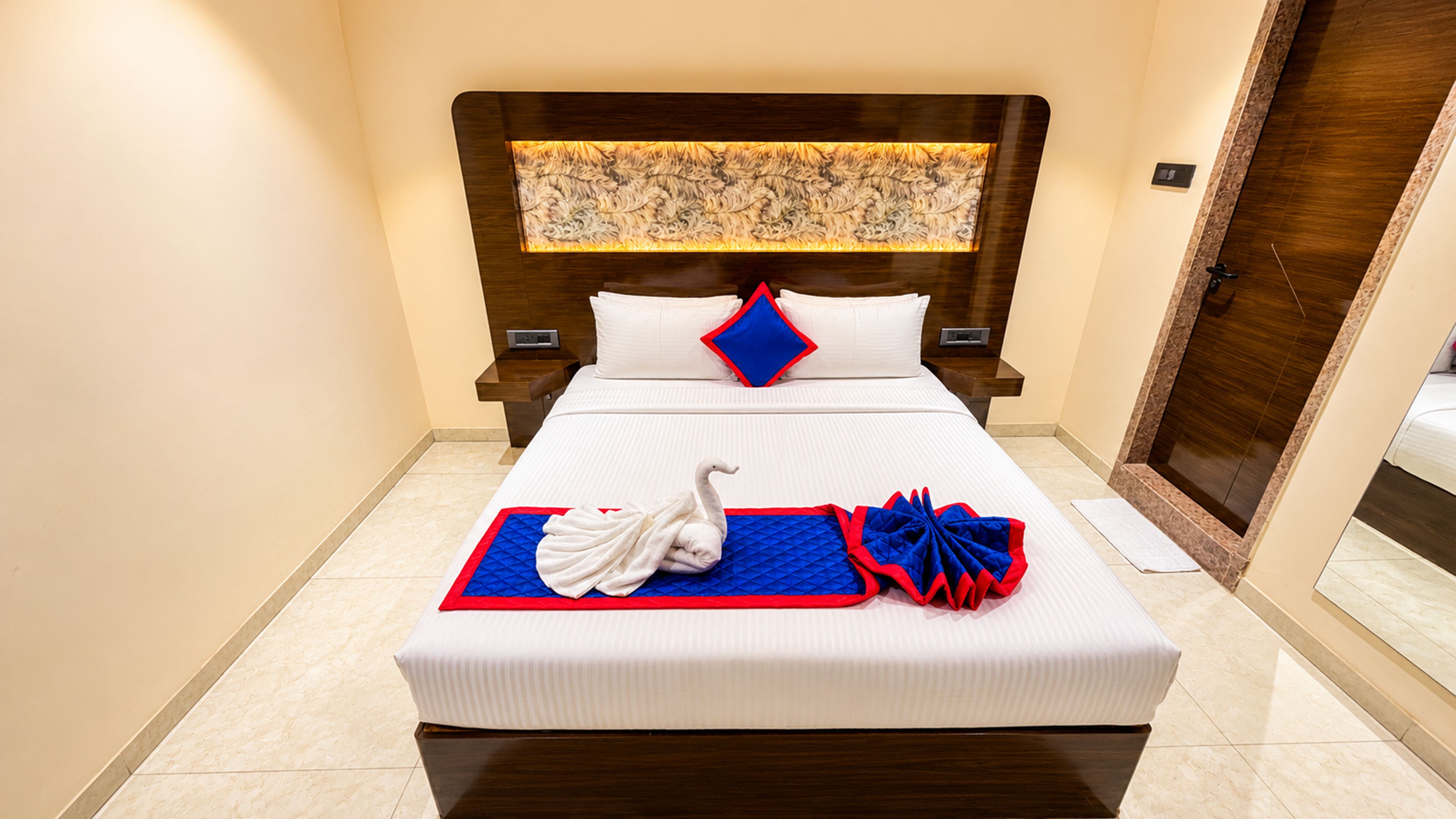 A hotel room with a large bed, a headboard with a decorative panel, a nightstand, and a door with a wooden frame.