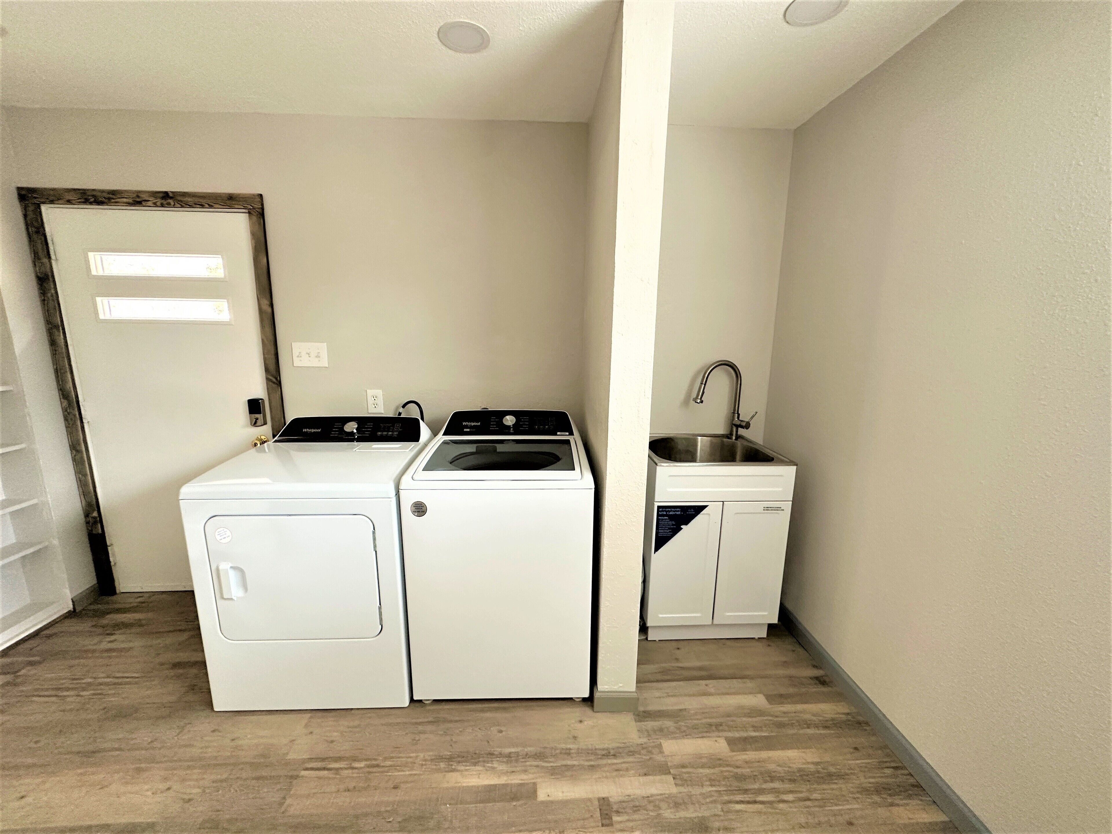 A laundry room with a washer and dryer, a sink, and a door with a light switch.