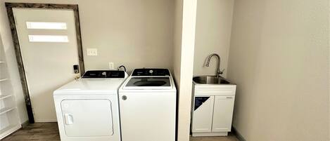 A laundry room with a washer and dryer, a sink, and a door with a light switch.