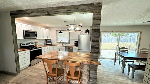 A modern kitchen with white cabinets, a wooden island, and a dining area with a table and chairs. - The Hideaway Oliver Springs, Only Min from Windrock Park (Oliver Springs)