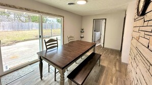 A dining area with a wooden table and bench, a sliding glass door to a patio, and a stone accent wall. - The Hideaway Oliver Springs, Only Min from Windrock Park (Oliver Springs)