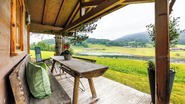 Eine Holzterrasse mit einer Bank, einem Tisch und Blick auf einen See und Berge.