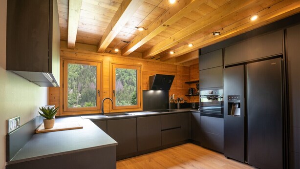 A modern kitchen with wooden ceiling beams, a built-in oven, and a large refrigerator.