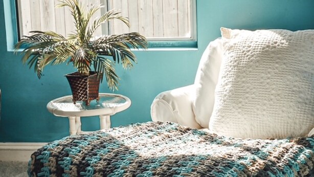Ein Zimmer mit einer türkisfarbenen Wand, einem weißen Stuhl mit weißem Kissen und einem kleinen runden Tisch mit einem Blumentopf.