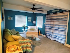 A living room with a ceiling fan, a sofa, a chair, a coffee table, and a patterned curtain.