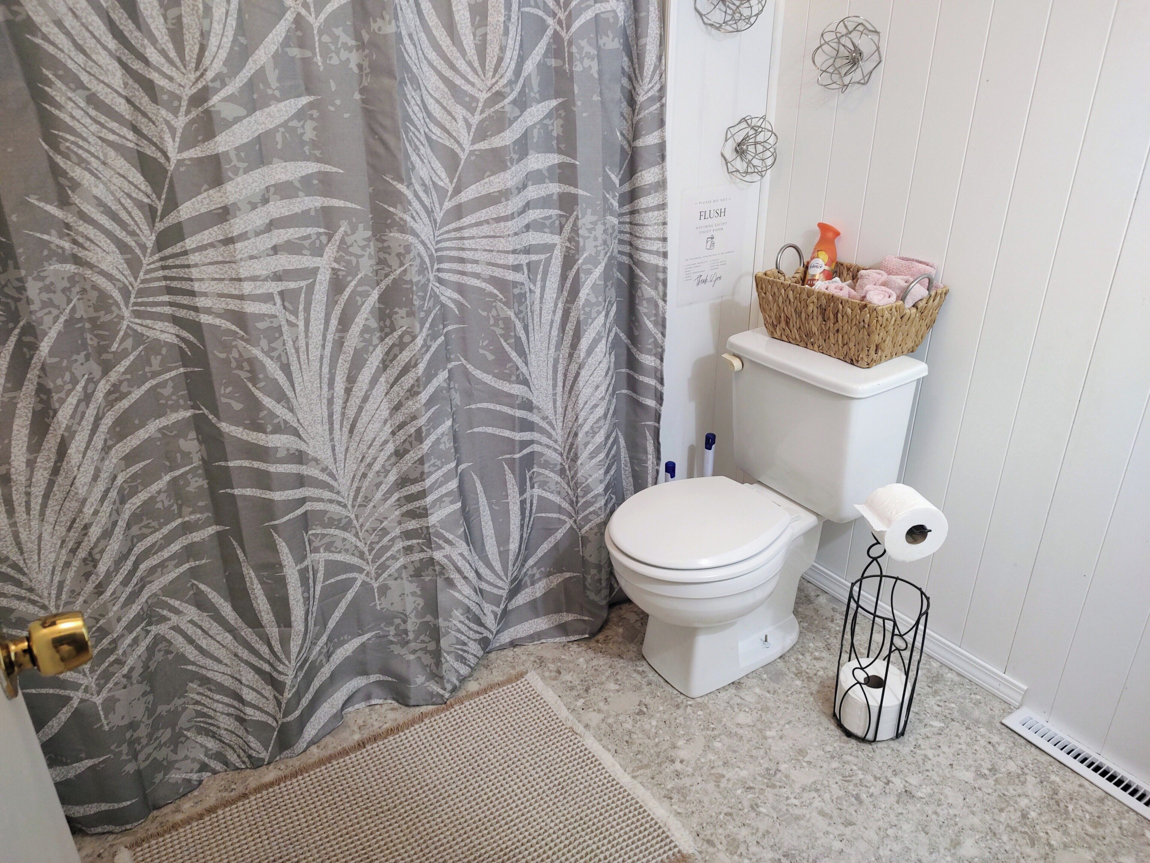 A bathroom with a toilet, a shower curtain, a basket with toiletries, and a roll of toilet paper.