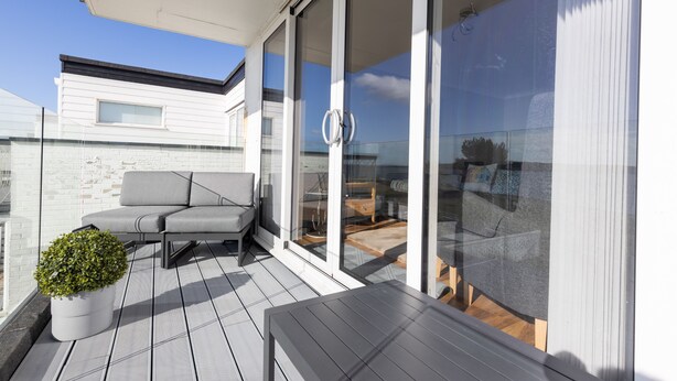Un balcon extérieur moderne avec un canapé gris, une petite plante en pot et une table en bois.