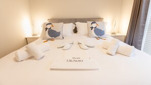 Un lit bien fait, avec un oreiller orné d’un motif d’oiseau, une paire de chaussons et une serviette sur laquelle est écrit « Linge à chaussures ».
