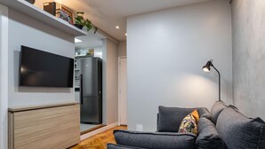 A modern living room with a grey sofa, a flat-screen TV, a built-in kitchen with a fridge, and a wooden floor. - Apartment in Copacabana Suite Bi204 (Rio de Janeiro)