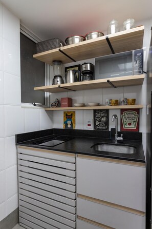 Uma cozinha com prateleiras de madeira, cafeteira, chaleira e pia.