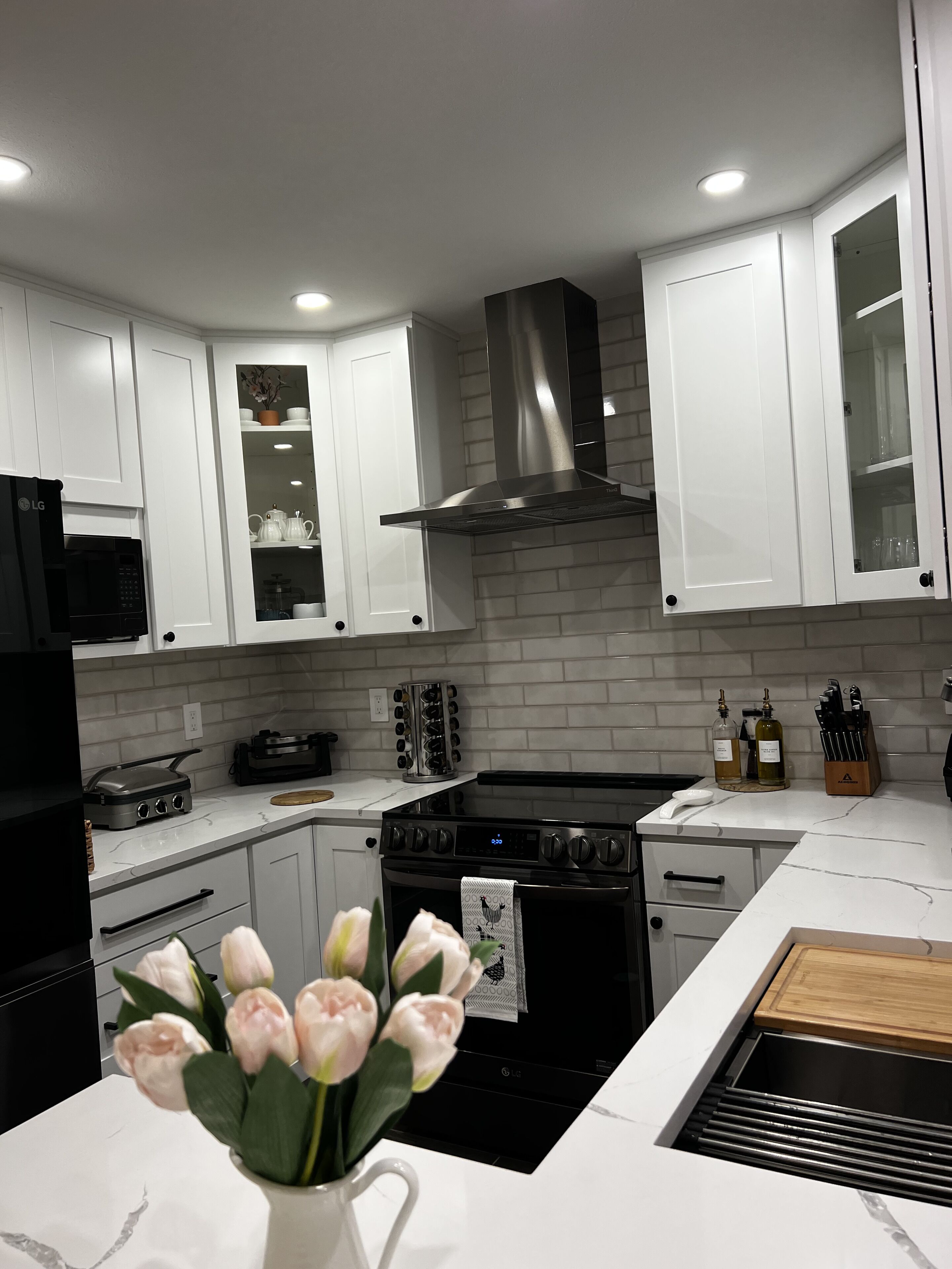 A modern kitchen with white cabinets, a stainless steel range hood, a black oven, and a marble countertop.