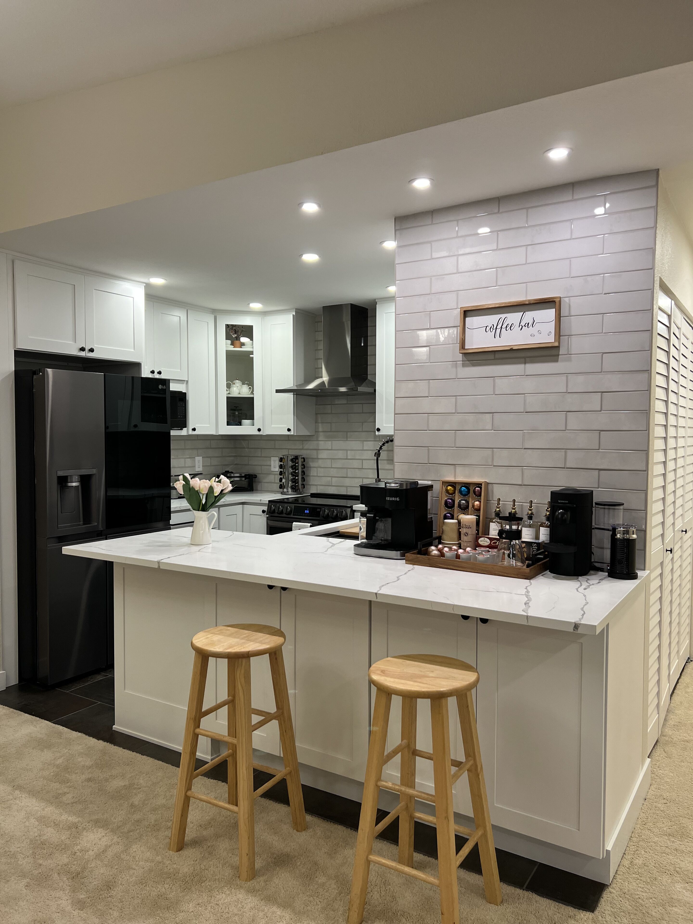 A modern kitchen with white cabinetry, a central island with stools, and a coffee bar sign.