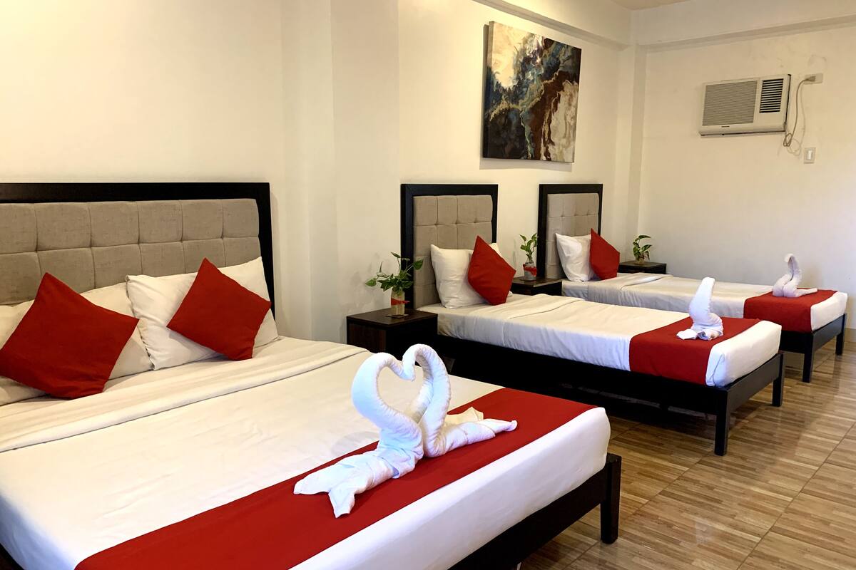 A hotel room with two beds, each with red and white bedding, and a swan-shaped towel on the beds.
