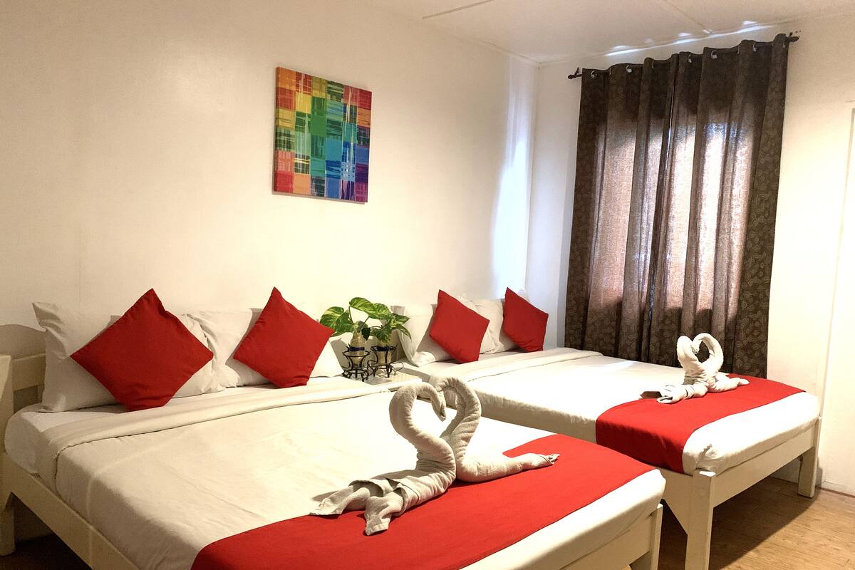 A hotel room with two beds, red pillows, a colorful abstract painting on the wall, and a curtain.