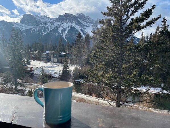 A mountain view with a cabin and a mug on a table. - Scenic Bliss Penthouse | Prime Location (Canmore)