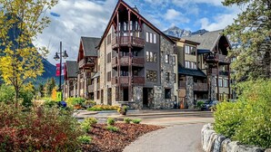 A multi-story hotel with stone and wood exterior, balconies, and a mountain backdrop. - Scenic Bliss Penthouse | Prime Location (Canmore)