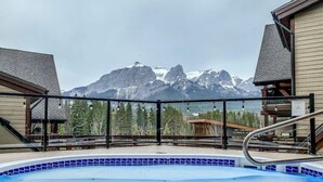 A hot tub with a mountain view, surrounded by a wooden deck and metal railing. - Scenic Bliss Penthouse | Prime Location (Canmore)