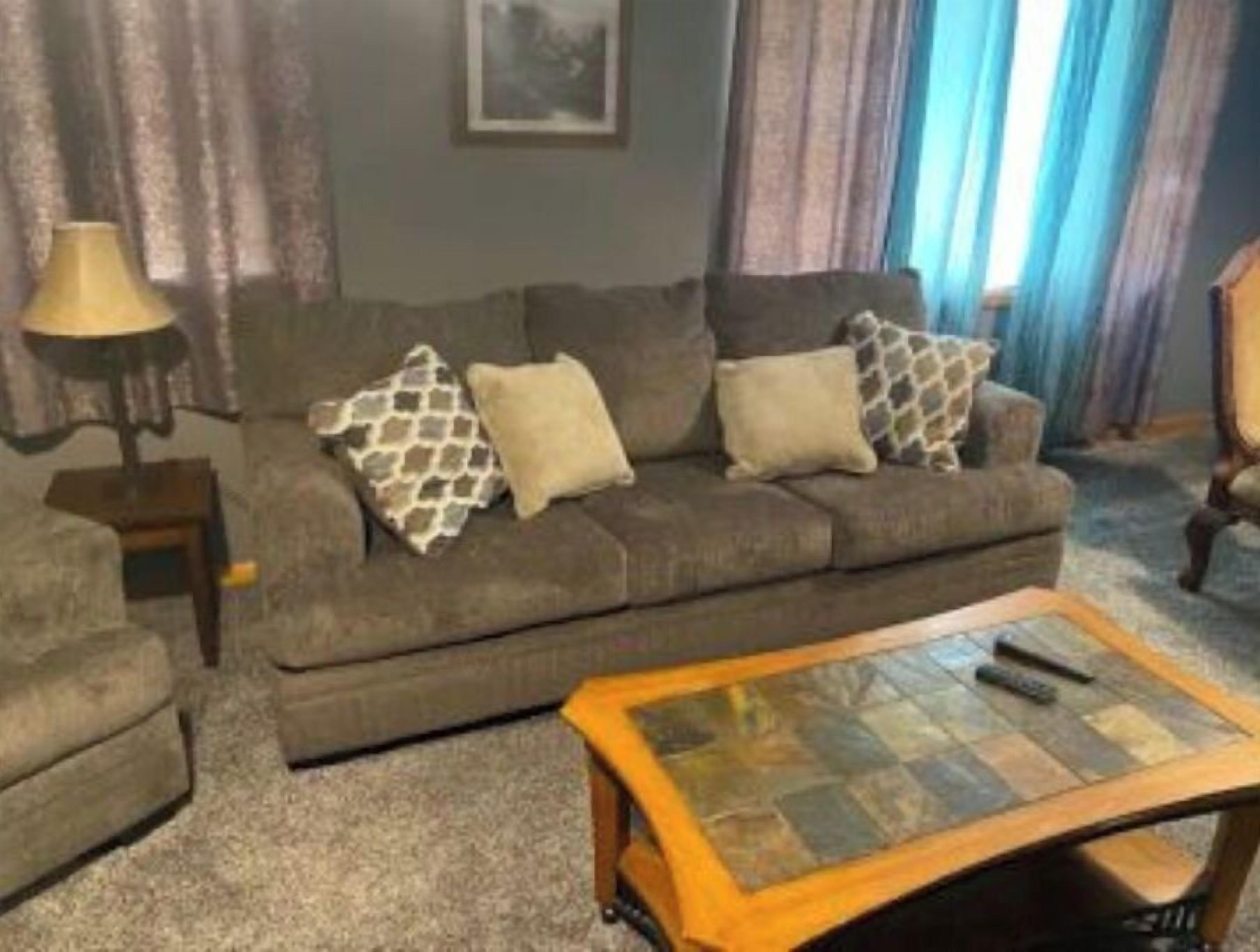 A living room with a grey sofa, patterned cushions, a wooden coffee table, and a lamp.