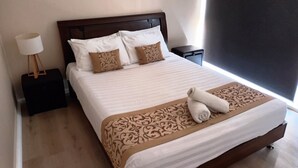 Una cama bien hecha con una colcha estampada y dos almohadones decorativos, una lámpara de noche y una mesita auxiliar.