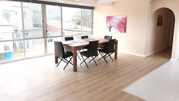 Un comedor espacioso con una mesa de madera y sillas negras, ventanas amplias con vistas al exterior y una obra de arte rosa en la pared.