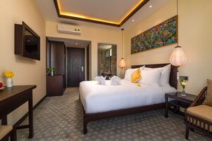 Habitación de hotel con una cama grande, un escritorio, una silla, un televisor montado en la pared y un cuadro sobre la cama.