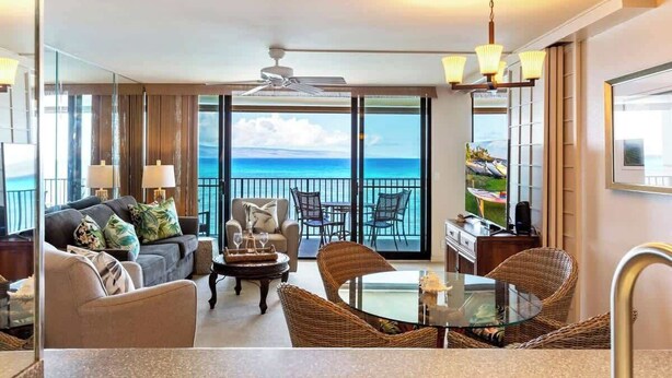 A spacious balcony with a view of the ocean, furnished with a sofa, chairs, and a table.