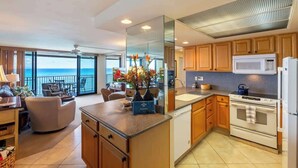 A modern kitchen with a view of the ocean, a dining area with a view, and a living room with a balcony.